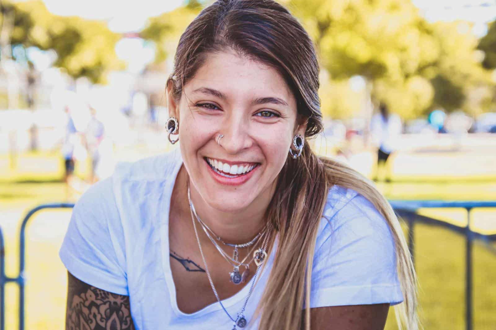Portrait of a smiling woman outdoors with tattoos and jewelry.