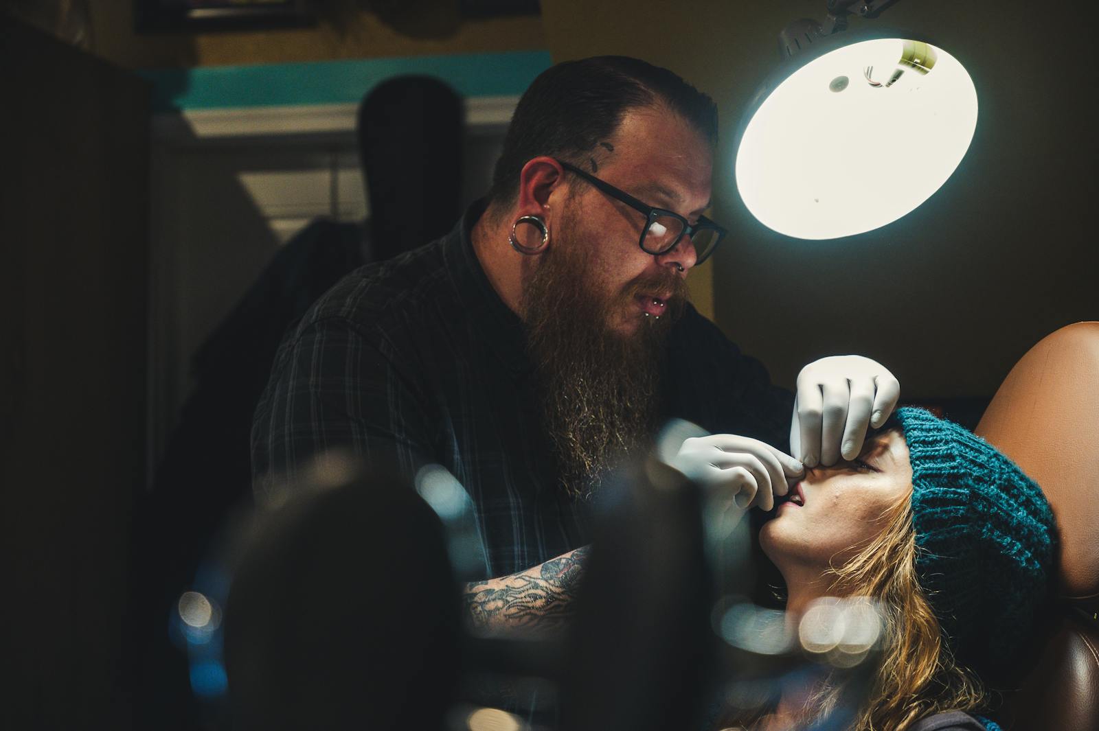 Professional piercer wearing gloves works on client in studio, focused on precision and detail.