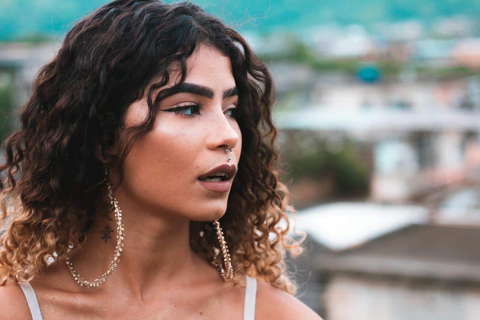 Close-up portrait of a woman with curly hair, earrings, and a nose piercing looking away.