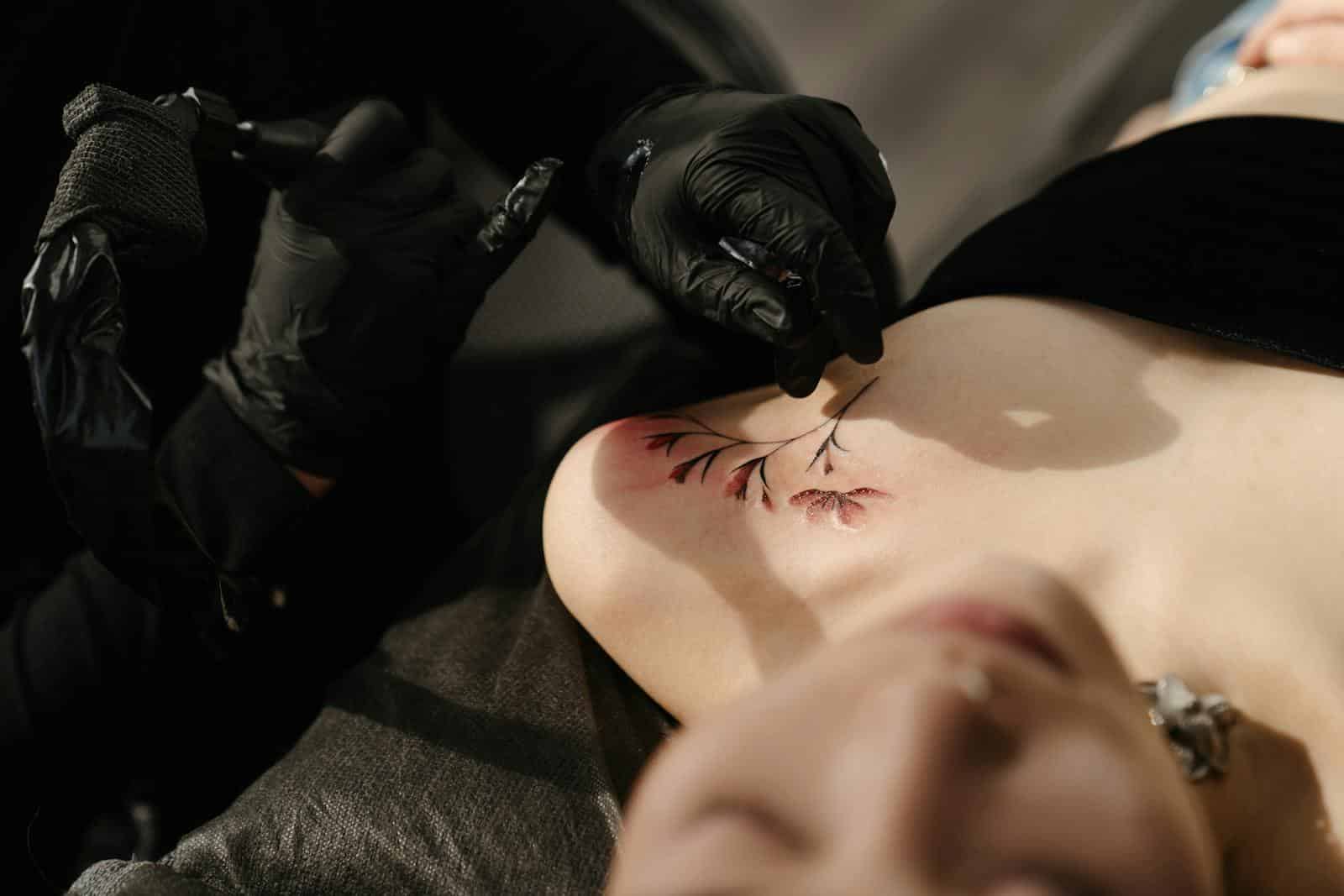 Close-up of a tattoo artist creating floral body art on a woman in a studio setting.