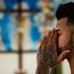 A man with tattoos prays inside a church, capturing a moment of reflection and spirituality.