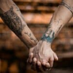 Close-up of tattooed hands holding each other, symbolizing connection and affection.