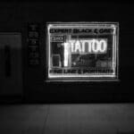 Monochrome image of a tattoo studio with a neon sign at night.