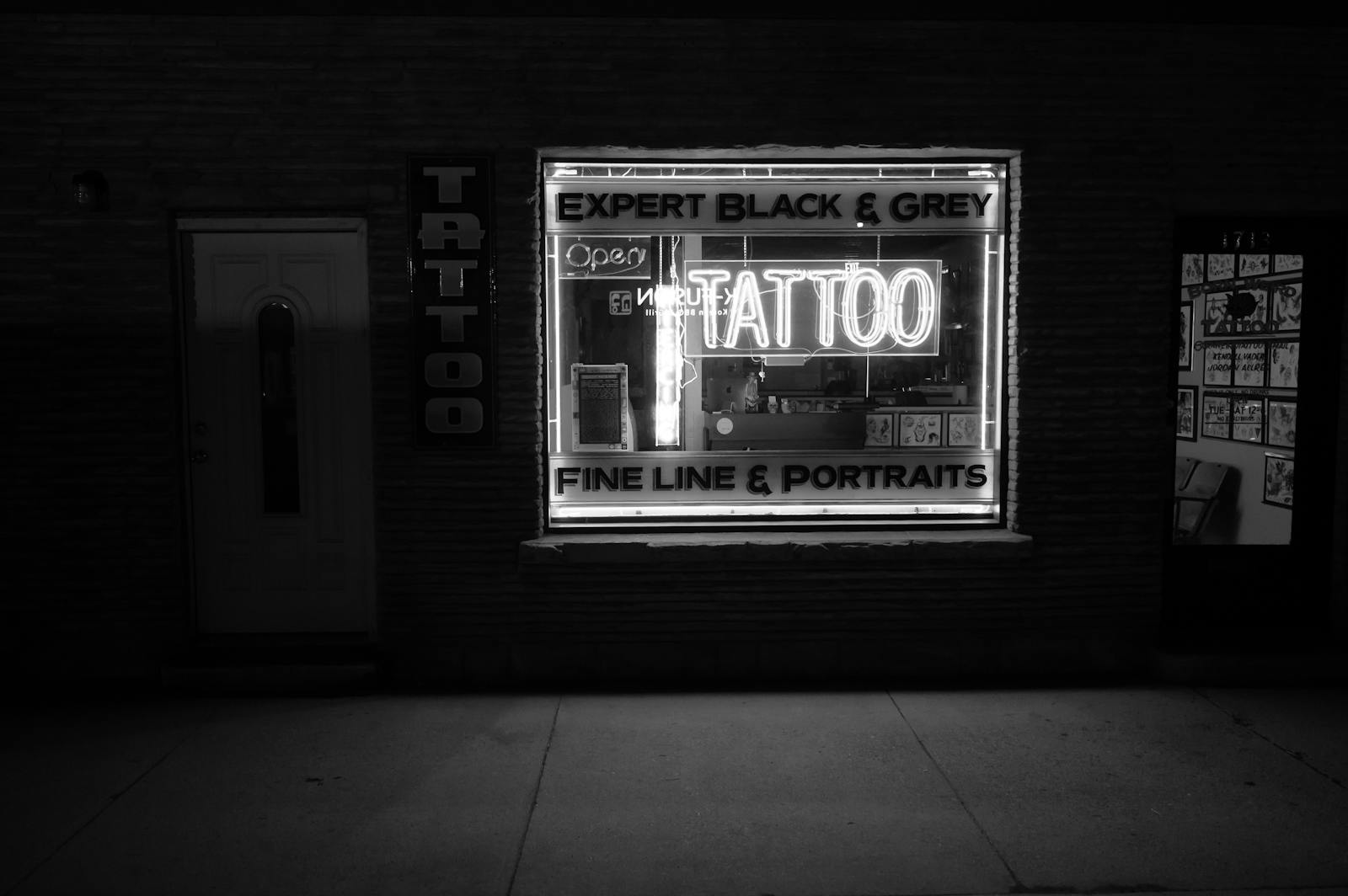 Monochrome image of a tattoo studio with a neon sign at night.