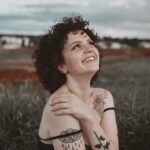 A smiling woman with tattoos enjoys the outdoors in Maringá, Brazil, exuding happiness and warmth.