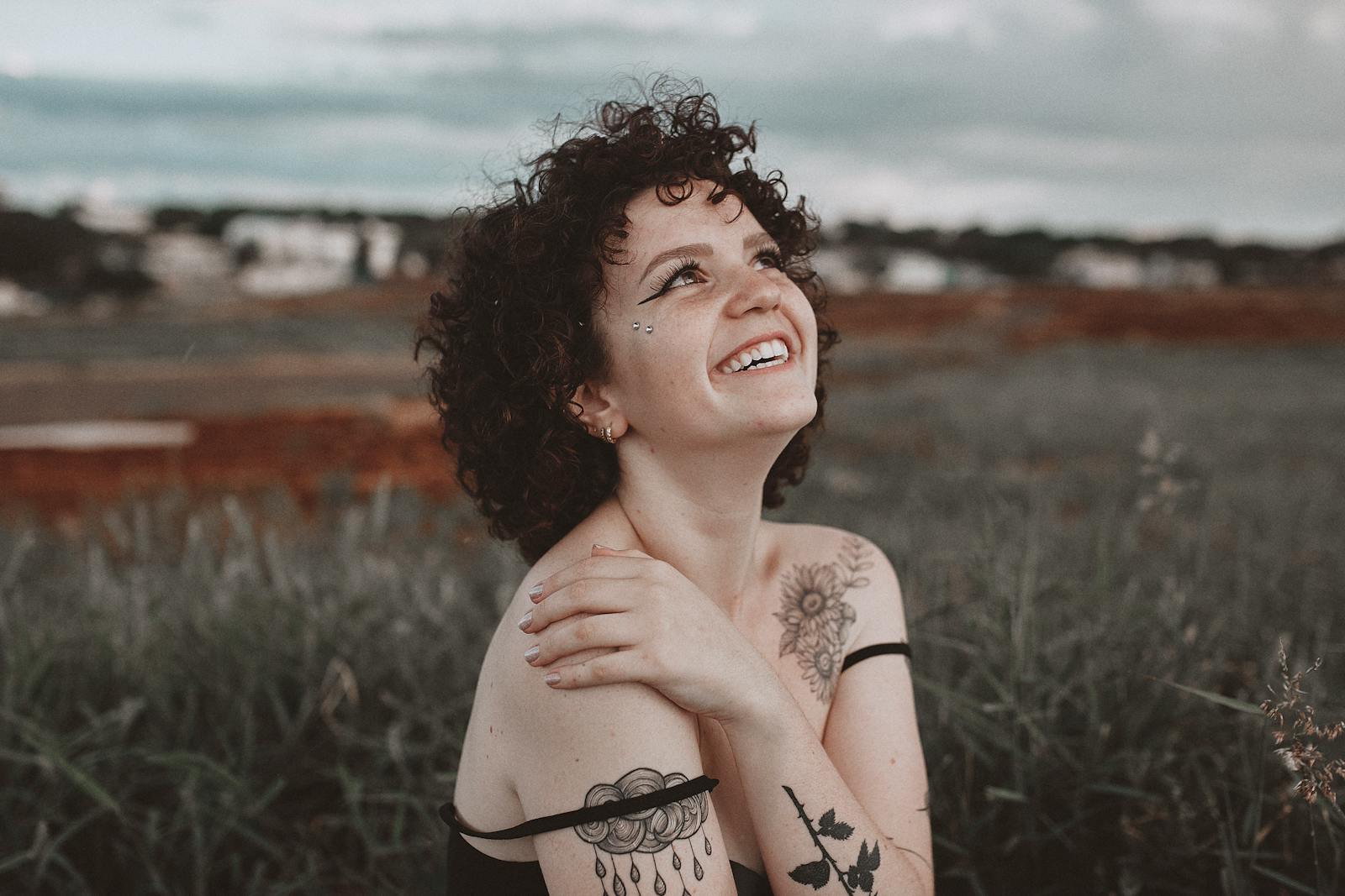 A smiling woman with tattoos enjoys the outdoors in Maringá, Brazil, exuding happiness and warmth.
