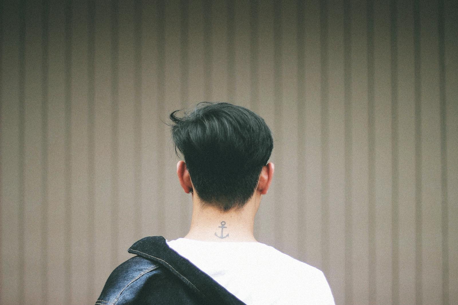 A man with an anchor tattoo on his neck seen from behind, wearing a jacket.