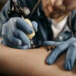 Tattoo artist working diligently on intricate design with tattoo machine and latex gloves.