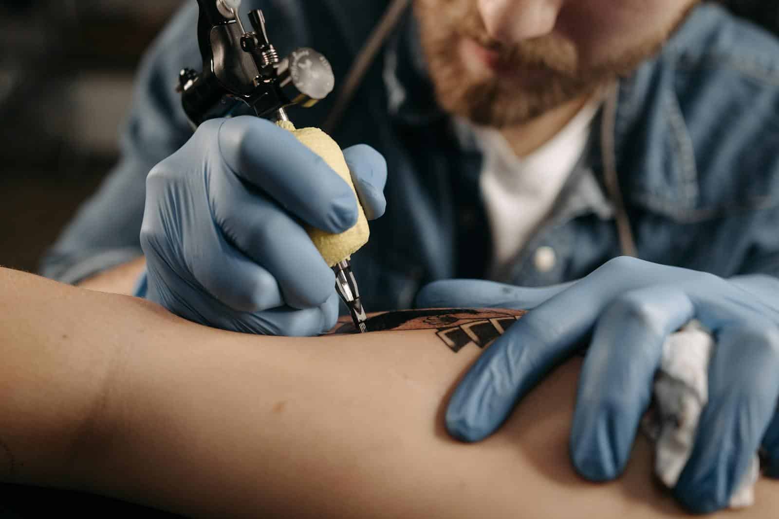 Tattoo artist working diligently on intricate design with tattoo machine and latex gloves.