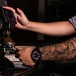 Close-up of a barista's tattooed arm using an espresso machine to grind coffee.