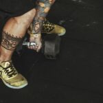 A tattooed individual lifting a dumbbell in a gym, showcasing fitness and style.