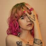 a woman with pink hair and tattoos holding her hands to her face