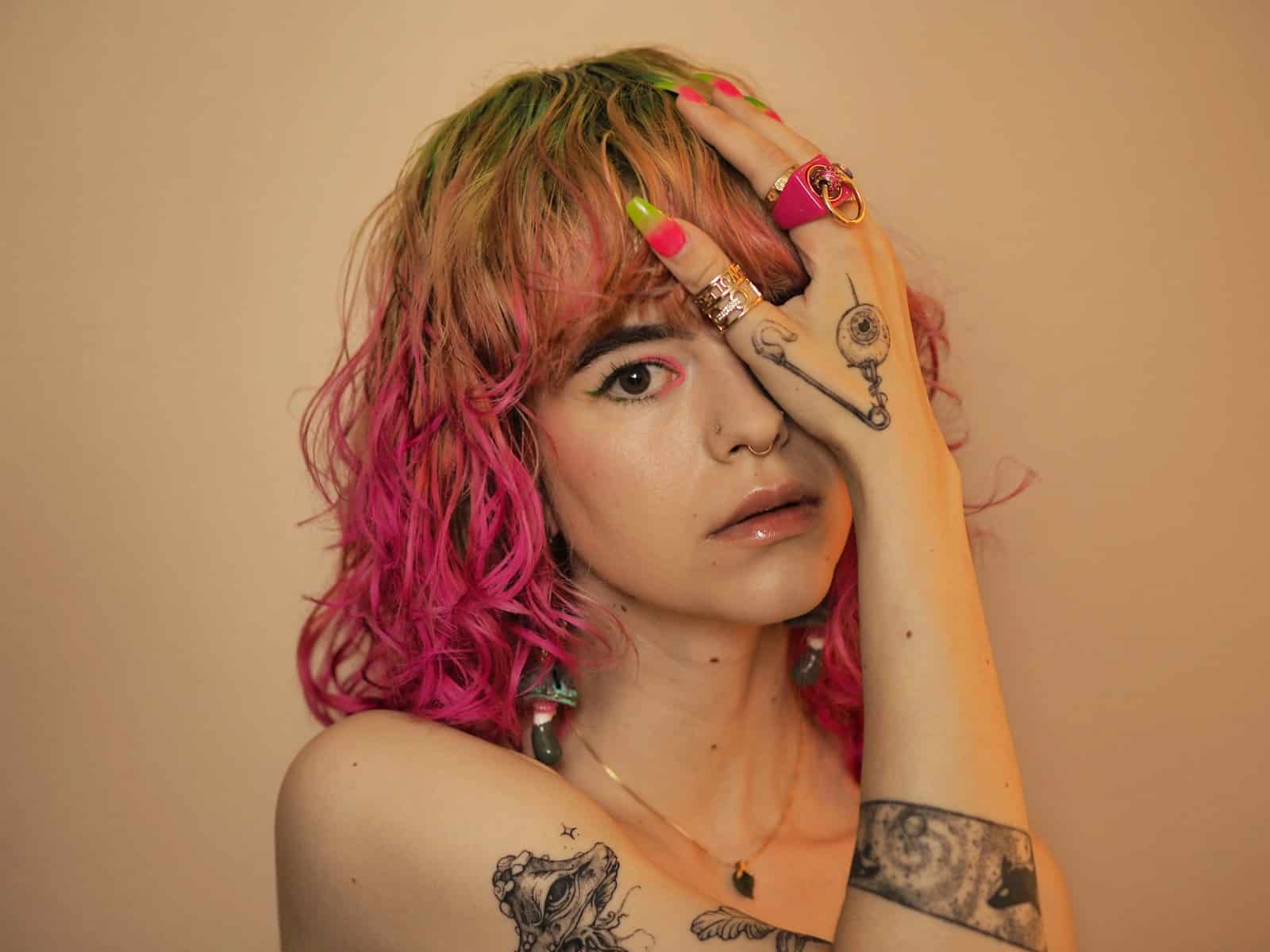a woman with pink hair and tattoos holding her hands to her face