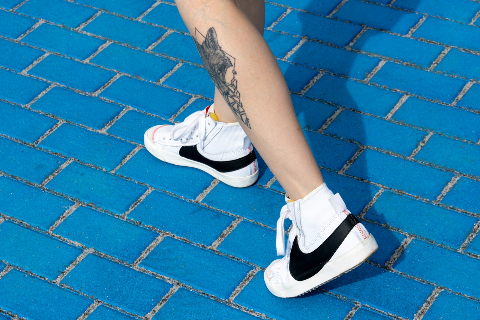 A person with tattoos standing on a blue brick sidewalk
